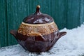 One brown ceramic pot covered with a lid stands on a table in white snow against a green wall Royalty Free Stock Photo