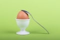 one brown egg in white egg cup before green background, a teaspoon is laying on it Royalty Free Stock Photo