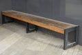 One brown wooden bench stands on the sidewalk near the gray metal wall Royalty Free Stock Photo