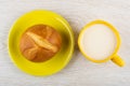 One bun in yellow saucer, cup of milk on table. Top view Royalty Free Stock Photo