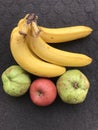 one bunch of bananas, two guavas and 1 apple on a dark background