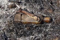 The burnt glass bottle lies in the ashes of an extinguished fire