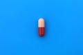 The drug in a two-color capsule lies alone on an isolated blue background. Royalty Free Stock Photo