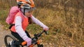 One caucasian children rides bike road in autumn park. Little girl riding black orange cycle in forest. Kid goes do Royalty Free Stock Photo