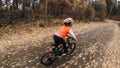 One caucasian children rides bike road in autumn park. Little girl riding black orange cycle in forest. Kid goes do Royalty Free Stock Photo