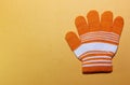 One children`s glove orange with white stripes lies on the yellow surface, fingers splayed, the ability to warm your hands in wint