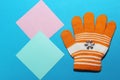 One children`s orange glove with white stripes lies on the blue surface, fingers splayed, the ability to warm your hands in winter