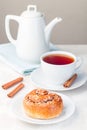 One cinnamon bun on a white plate, served with cup of red tea, vertical