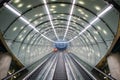 One cleaning staff person in orange coat on escalator at modern, futuristic architecture subway station, arched ceiling