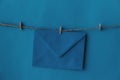 One closed blue envelope hanging on rope isolated blue background.