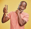 One contemplative trendy mature African American man taking selfies on a cellphone against a yellow studio background
