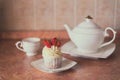 One cupcake with white cream decorated with fresh strawberries on the table, accompanied by a white teapot and cup Royalty Free Stock Photo