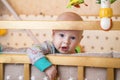 One curious caucasian infant baby boy with blue eyes is trying to climb out from child crib