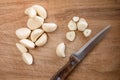 One cut and many uncut peeled cloves of garlic on a wooden cutting board and a knife Royalty Free Stock Photo