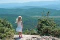 One cute blonde girl in countryside on a high rock among the mountains on a bright sunny day