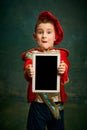 One cute little boy dressed up as medieval little prince and pageboy using tablet over dark vintage style background