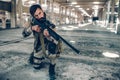 One dark-haired man is standing in long hangar by himself. He has put one knee down on the ground and holding rifle in Royalty Free Stock Photo