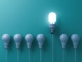 One eco energy saving light bulb glowing and standing out from unlit incandescent white bulbs on green pastel color wall backgroun Royalty Free Stock Photo