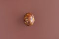 One egg, painted in brown colors, on brown background. Minimalism concept. Unusual pattern on surface of egg in form of spots
