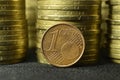 One euro cent coin placed on edge in front of piles of coins