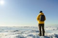 One Faceless Man In Yellow Raincoat With Backpack Standing On Frozen Sea. Nature