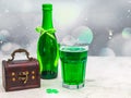 One faceted large glass with green beer white foam, a bottle with a ribbon and a wooden chest