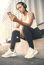 One fit young hispanic woman listening to music with headphones from a cellphone while taking a break from exercise Royalty Free Stock Photo