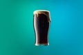 One full glass of frothy dark beer isolated over gradient blue and green color background in neon. Concept of alcohol