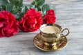 One gilded cup of coffee and three red roses Royalty Free Stock Photo