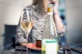 One glass and bottle of white champagne or prosecco on table with blurred portrait of young adult female person drinking alone. Royalty Free Stock Photo