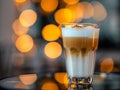 One glass cup of coffee latte macchiato with cinnamon-sprinkled foam on the table in the cafe. Blurred background