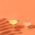 One glass have two aronia berries on top of it. Two posh crystal glasses with yellow cocktails against orange background. Moody