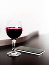 One glass of red wine and a mobile phone on brown wodden table and white blurred wall background. Alcohol drink and smartphone on Royalty Free Stock Photo