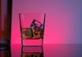 One glass of whiskey with ice cubes near bottle on table with reflection, lights disco atmosphere Royalty Free Stock Photo