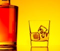 One glass of whiskey with ice cubes near bottle on table with reflection, warm tint atmosphere Royalty Free Stock Photo