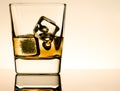 One glass of whiskey with ice cubes on table with reflection, light brown atmosphere Royalty Free Stock Photo