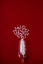 One glass with white hearts on red background. Valentine's Day, love concept. Copy space. Vertical orientation Royalty Free Stock Photo