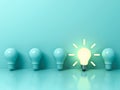 One glowing idea bulb standing out from unlit incandescent bulbs on light green pastel color background
