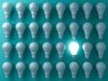 One glowing light bulb standing out from the unlit or dim bulbs on dark green pastel color background Royalty Free Stock Photo