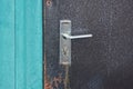 One gray metal doorknob on a brown iron dirty door and a green wall