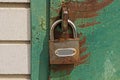 One gray metal padlock hangs on an iron green door in brown rust Royalty Free Stock Photo