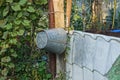 One gray zinc bucket hangs on a wooden board near a well