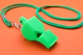 One green whistle with cord on orange background, closeup