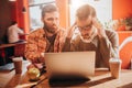 One of the guys is upset and looking to the screen of laptop while another one is to his friend with hope and saddness.