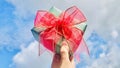 Holding a green Christmas gift with a red ribbon against the blue sky and white clouds background. Royalty Free Stock Photo