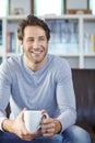 One handsome smiling man sitting alone on his sofa in his living room and drinking coffee. Mature man feeling happy Royalty Free Stock Photo