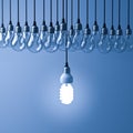 One hanging eco energy saving light bulb glowing and standing out from unlit incandescent bulbs on dark blue background Royalty Free Stock Photo