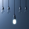 One hanging energy saving light bulb glowing different stand out from unlit incandescent bulbs