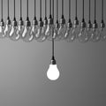 One hanging light bulb glowing different and standing out from unlit incandescent bulbs on dark grey background Royalty Free Stock Photo
