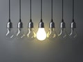 One hanging light bulb glowing different and standing out from unlit incandescent bulbs Royalty Free Stock Photo